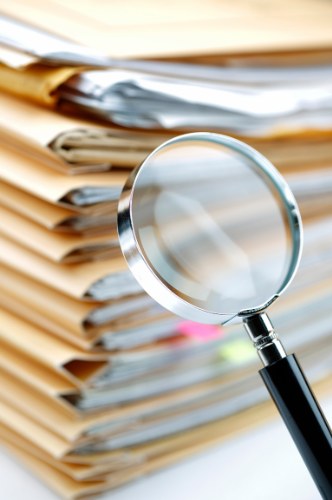 Stos dokumentów ISO analizowanych lupą – dokumentacja systemów zarządzania ISO